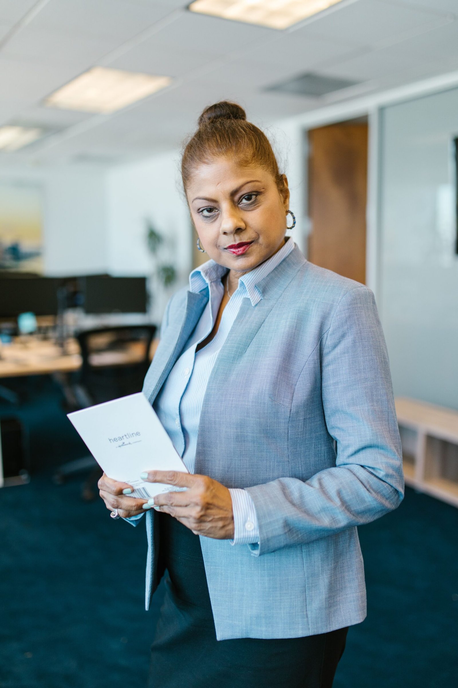 Confident businesswoman in office holding a document, showcasing professionalism and leadership.